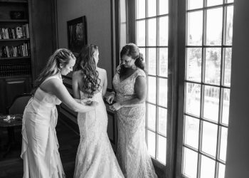 a black and white photo of a bride with her bridesmaids helping her get ready