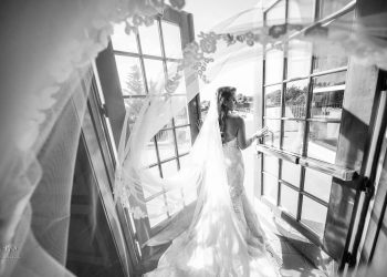 a black and white photo of a bride walking through french doors leading to the outside