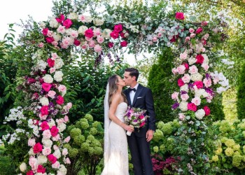 a bride and groom outside, kissing infront of a canopy of flowers