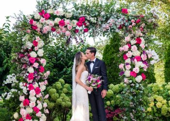 a bride and groom outside, kissing infront of a canopy of flowers