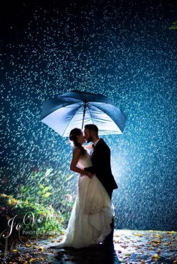 a bride and groom outside, in the rain, under an umbrella