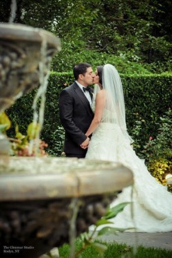 a bride and groom kissing, behind a fountain