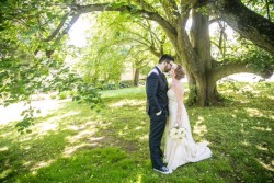 a bride and groom outside, kissing under a large tree