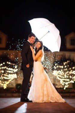 a bride and groom taking a photo outside, under an umbrella