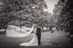 a black and white photo of a bride and groom outside with trees around them