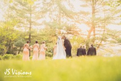 a bride and groom kissing, outside surrounded by trees and their wedding party