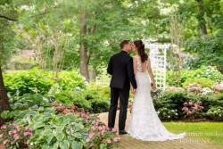 a bride and groom outside, kissing, surrounded by foliage